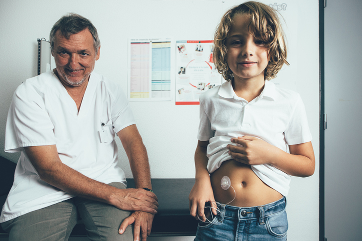 Child posing with insulin pump next to his doctor in the doctor's office