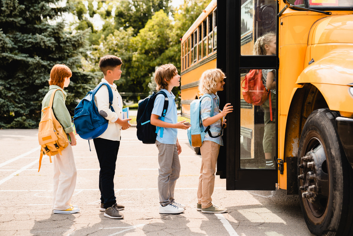Children wearing backpacks getting on a school bus