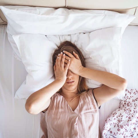 Woman looking disappointed laying in bed with hands covering her face