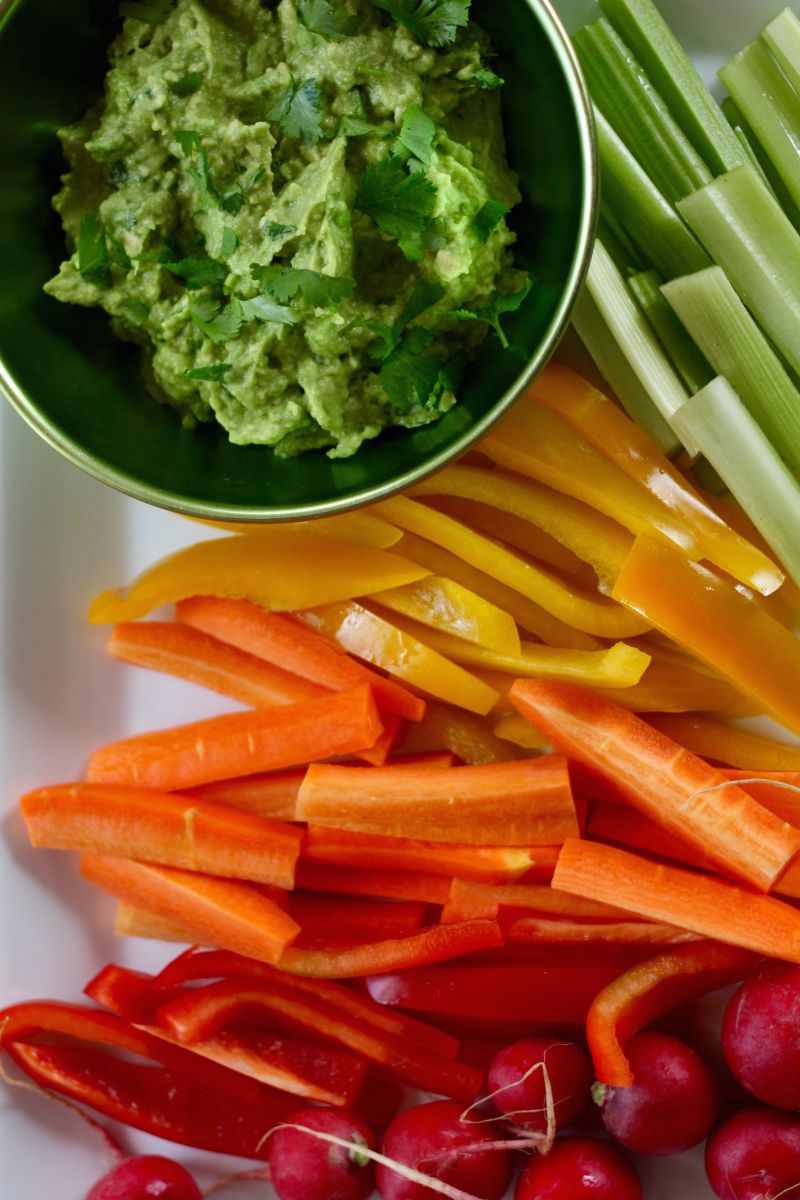 Guacamole beside celery, sliced bell peppers, sliced carrots, and radishes