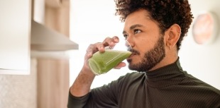 man drinking glass of green juice
